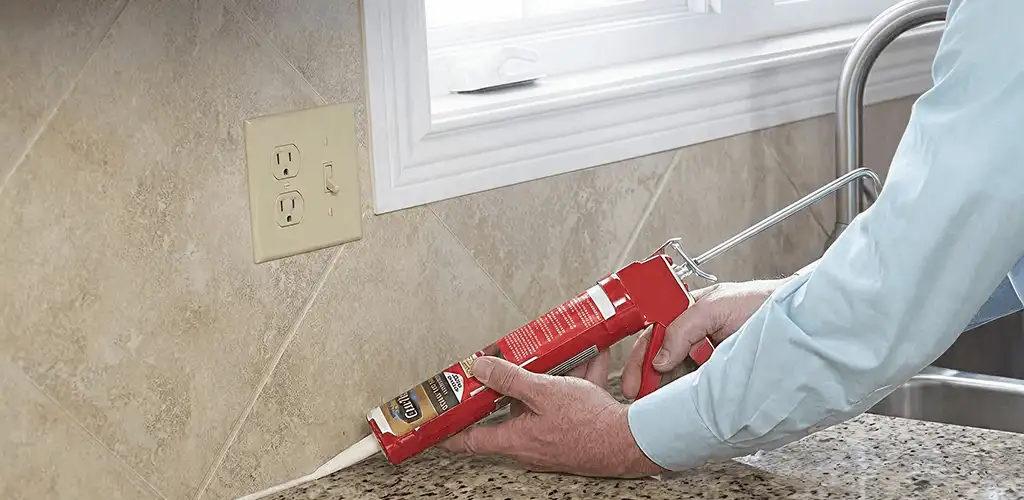 Handyman applying caulk along a kitchen backsplash and countertop seam in Milwaukee, WI